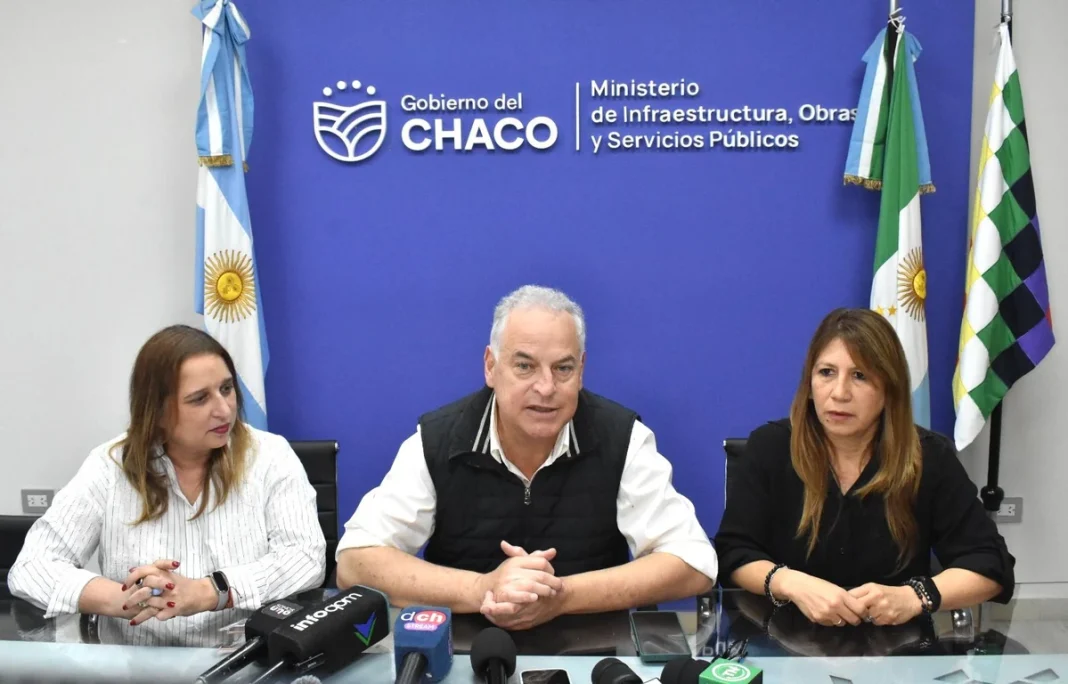 Hugo Domínguez durante una conferencia acompañado por dos funcionarias, frente a las banderas del Chaco