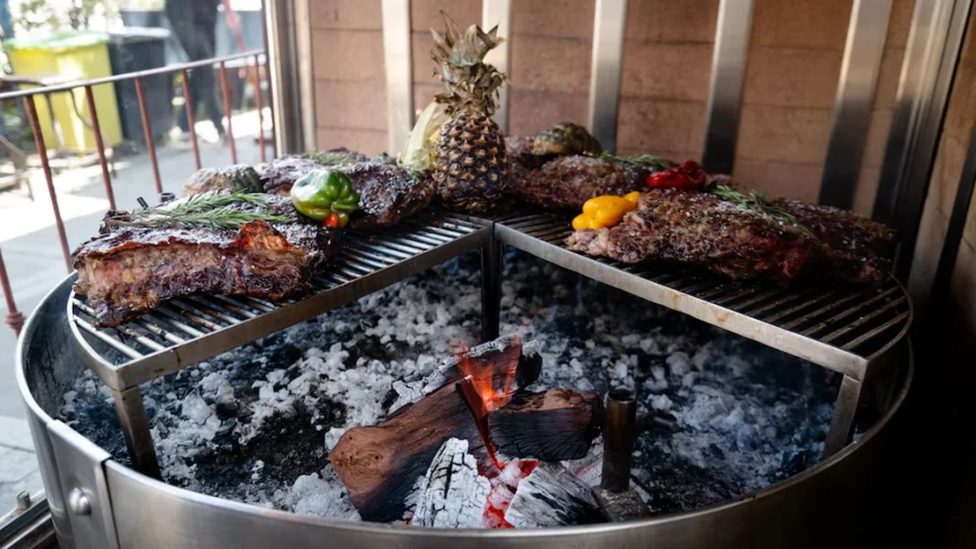 Cortes de carne cocinándose sobre una parrilla con carbón y leña