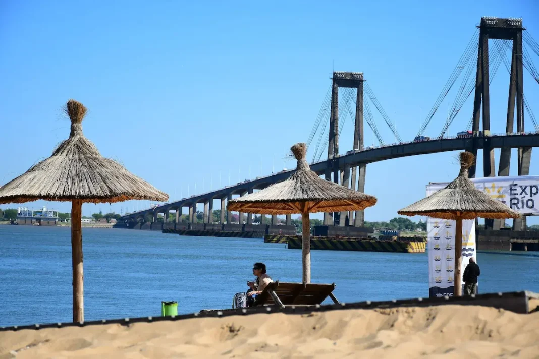 Personas en una playa de Corrientes junto al Paraná y un puente al fondo