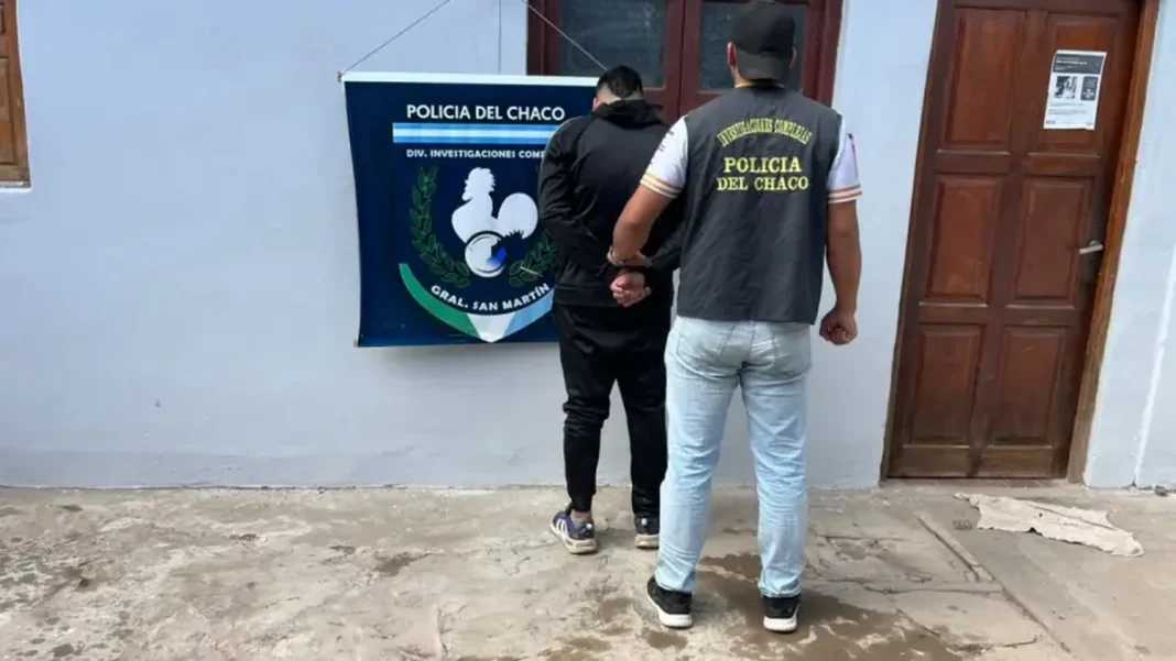 Un efectivo de la Policía del Chaco acompaña a un hombre frente al emblema policial de General San Martín.